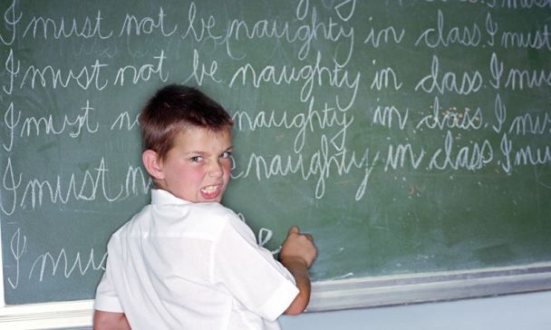 A schoolboy writing lines on a blackboard