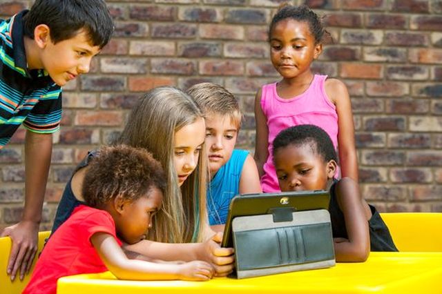 Multiracial group of children looking at tablet outdoors.