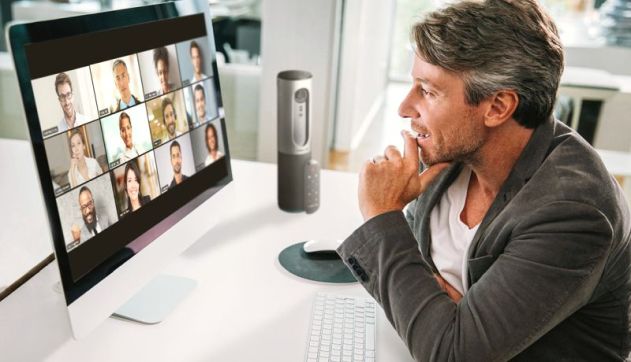 man at his desk interacting with a zoom meeting showing on a lar